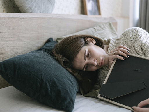 Woman in bed holding a picture frame, represents how grief & loss therapy can help you move on while honoring your loss.