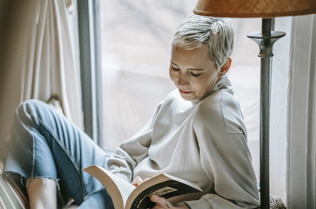 Woman reading a book by the window, represents our selection of best grief books for adults to help you navigate loss.