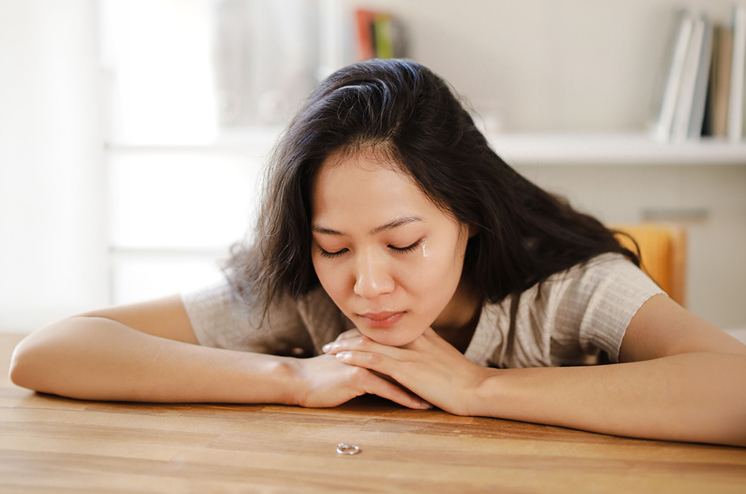 Woman crying while looking at a wedding ring, represents the trauma from being cheated on and how to start healing.
